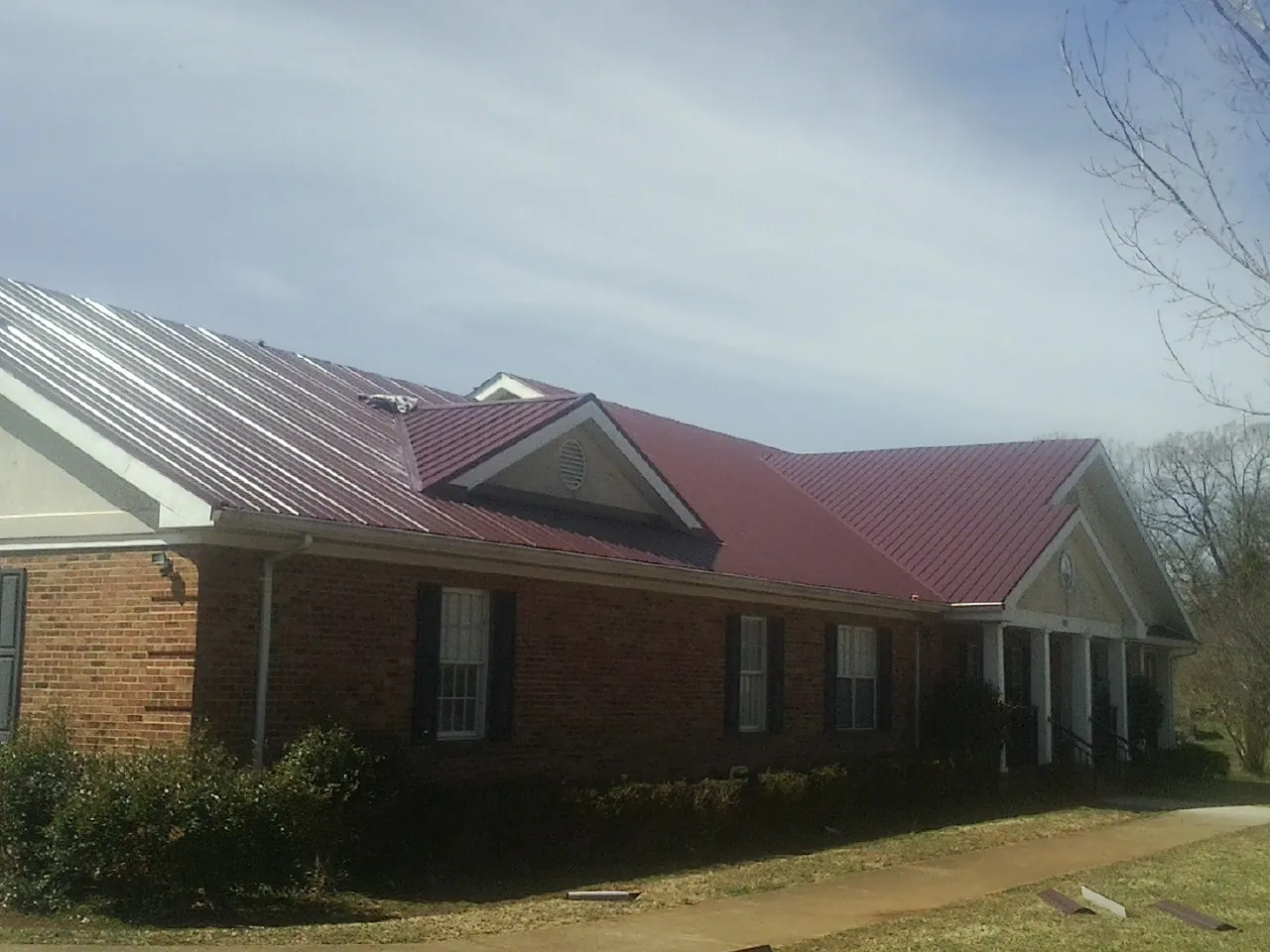 Red metal roof with gabled entries on a long brick building, from a Hail Damage Roof Repair job in Port Hueneme Cbc Base
