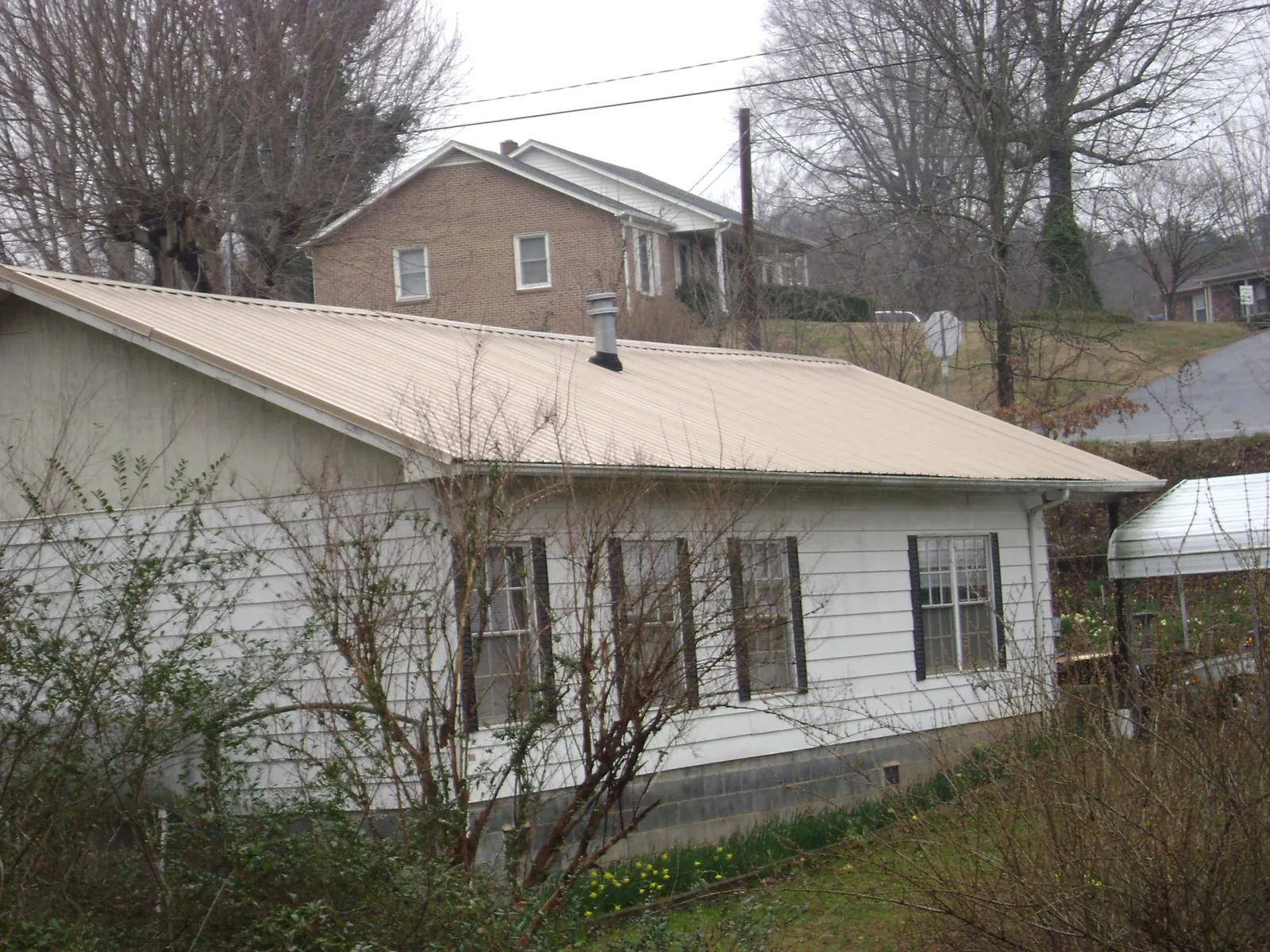 Tan metal roof on a white sided house set into a hillside — Commercial Roofing by Roofing Brothers in Port Hueneme Cbc Base